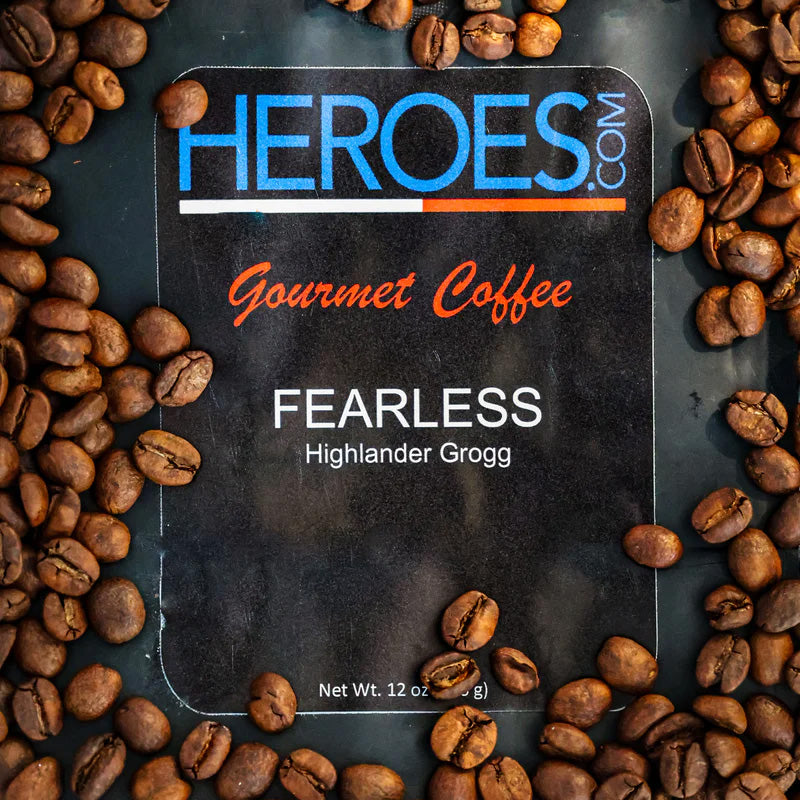 A bag of HEROES.com Gourmet Coffee labeled FEARLESS Highlander Grogg, surrounded by scattered coffee beans. The bag shows the net weight as 12 oz (340 g).