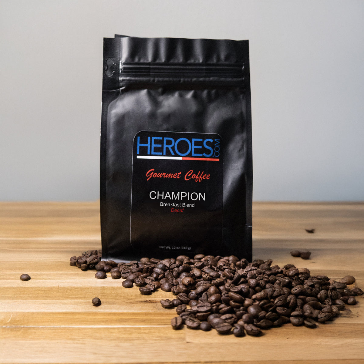 A black bag of CHAMPION Breakfast Blend (Decaf) sits on a wooden surface with coffee beans in front. The label highlights that it’s made from premium Arabica beans and is completely caffeine-free.