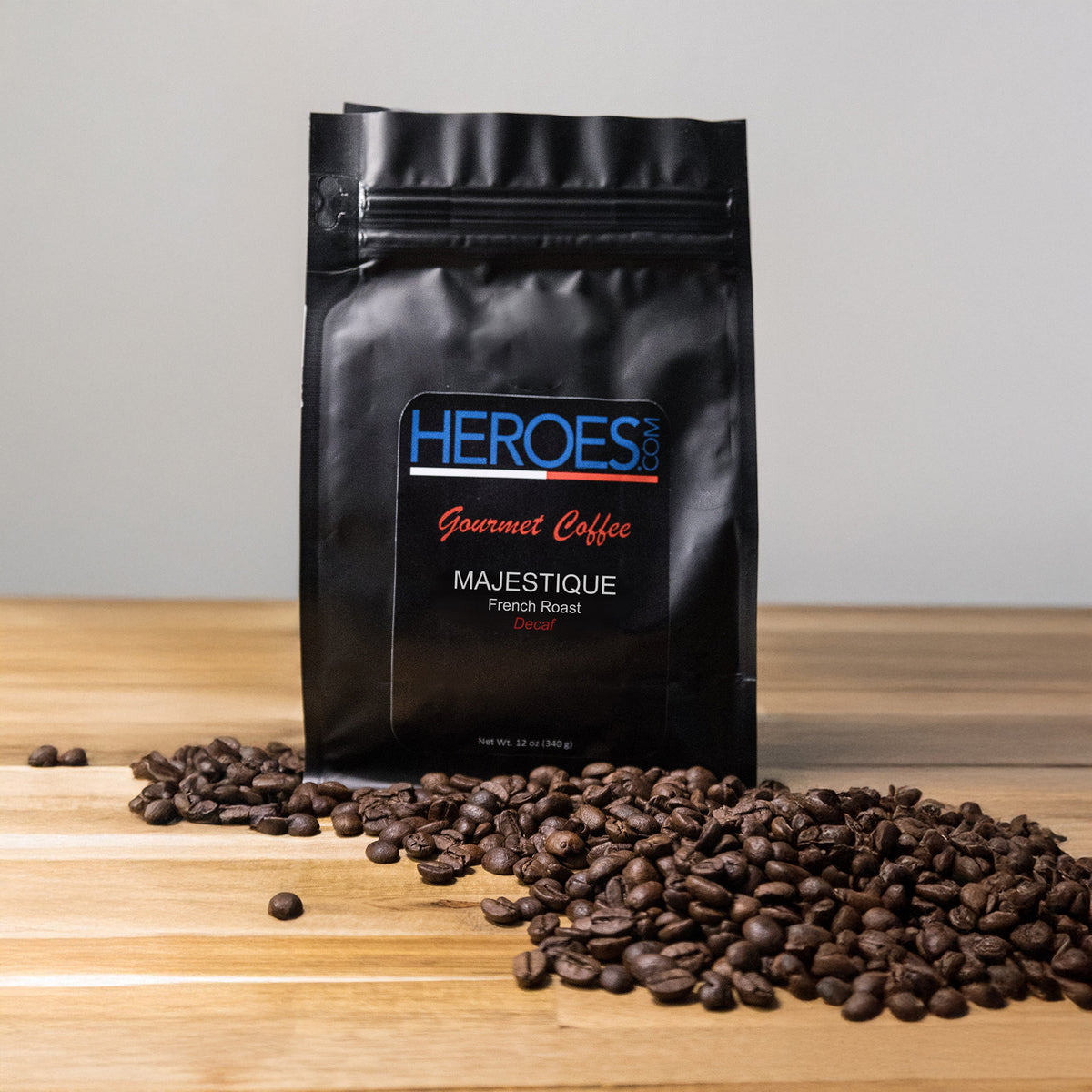 A black bag labeled MAJESTIQUE French Roast (Decaf) stands upright on a wooden surface amid coffee beans, showcasing this delicious dark roast decaf made from premium Arabica beans.